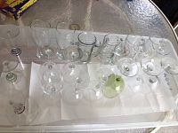 Top-down image of assorted wine glasses, beer mugs, and martini glasses on a paper towel inside a plastic tub.