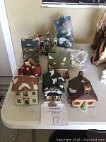 Photo of the 8 Christmas village buildings arranged on a table with light cords and small trees, showing various building types.