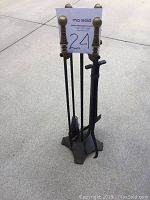 Set of four fireplace tools and the stand on concrete floor, visible brass ball handles and triangular base.
