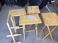 Four light wood TV trays arranged around their stand, showing surface wear and discoloration.