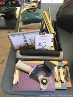 View of desk supplies including label maker, rulers, stapler, tape dispensers, clipboards, and small tools.