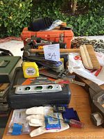 Various small hand tools such as measuring tape, level, screwdrivers, brushes, gloves, toolboxes, chains, and truck hitch ball displayed on table