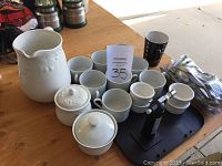Overview of ceramic pitcher, coffee cups, lidded jars, espresso cups, black tray, torch lighter, and silverware on wooden table