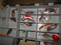 Partial inside view of the fishing satchel showing metal spoons, colorful lures, and some fishing flies with hooks.