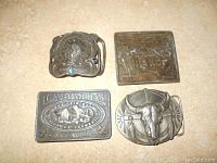 Four vintage belt buckles displayed on a beige surface, showing front details and design elements.