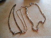 Three silver necklaces laid out on surface, showing different chain styles and lengths