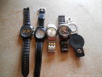 Five older watches lined up showing different strap materials and dial designs, including a pocket watch in leather case.