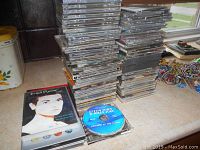 Photo showing a large stacked pile of numerous music CDs in jewel cases with visible titles and artwork from various artists.