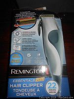 Box showing Remington Essentials Plus Hair Clipper branding and features including titanium coated blades, powerful motor, taper lever, and 22 pieces included.