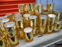 Front view showing a group of reflective gold mercury glass votive holders with speckled silver patterns inside, some with used white candles inside.
