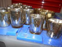 21 silver and miscellaneous mercury glass votive holders arranged together showing a variety of sizes and finishes.