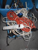 Bin containing miscellaneous electrical items: extension cords, power strip, various wires and chargers tangled together.