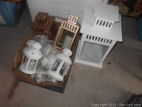 Nine lantern candle holders including white metal lanterns with star cutouts, natural wood-tone lanterns, and a tall white metal lantern, some with glass panels and one with a candle inside.