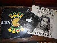 Photo showing all three vinyl records: Peter Tosh Wanted LP sealed with hang hole, Tuff Gong Rita Marley LP sleeve, and L.L. Cool J 45 single.