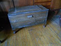 Front view of rustic wooden storage chest showing hinged lid, metal handles, and cast iron claw feet legs.