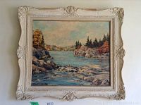 Full view of the framed oil painting showing a river scene with rocks and trees under a partly cloudy sky.