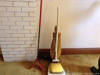 Photo showing vintage Hoover vacuum with yellow cloth bag, Shark vacuum in background, and red-handled Vileda brush leaning against wall