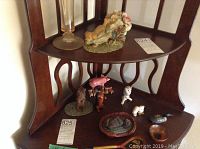 Photo of wooden shelf displaying various ceramic animal figures (pigs, dogs, bird) and ceramic flower arrangement with tall glass vase on top shelf