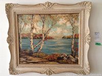 Full frontal photo of oil painting with ornate cream frame depicting river scene with birch trees and rocks.