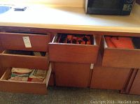 Five wooden drawers with various kitchen items such as flatware and utensils inside.