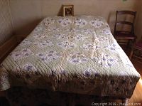 Full bed setup with mattress covered by quilted floral bedspread on frame