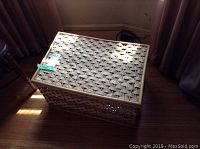 Closed wicker chest in a room with wooden floor and curtains nearby, showing natural light shadows.