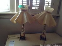 Pair of pleated cream plastic lampshades on metal and plastic based lamps atop a surface near a window.