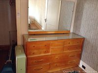 Wood dresser with protective glass top, showing the front side with multiple drawers and wooden knobs and handles.