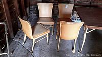 Four vintage style dining chairs with metal frames and tan vinyl upholstery arranged in a group. Chair seat and back surfaces show discoloration and damage.