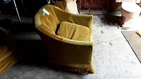 Side view of mustard yellow fabric upholstered armchair showing curved arms, tufted backrest, and pleated skirt base upholstery.
