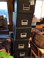 Stack of five black bankers boxes with label holders, stacked vertically near a window.