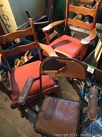 Two wooden armchairs with reddish vinyl seats, curved armrests, horizontal slat backrest. A folding chair with damaged brown vinyl seat and backrest in front.