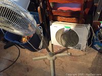 Side view of a 14-inch floor fan with adjustable height and three-legged base alongside a rectangular white Duracraft window fan.