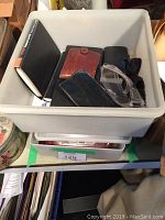 Bin with men's leather wallets, card files, and eyeglasses in protective cases as seen from above