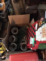Box containing twelve white boat trailer rollers along with a wooden Santa themed board and tangled Christmas light string.