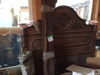 Antique solid wood bed frame headboard and footboard with carved details and quatrefoil cutout on headboard, side rails bundled together, displayed indoors.