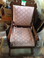 Front view of wooden rocking chair with pink patterned seat cushion and carved wood details on backrest.
