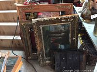 Two ornate wooden frames with one displaying an oil painting, four vintage metal organizer panels in the background.