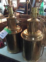 Pair of cylindrical brass lamps with sockets and cords, showing overall shape and size.