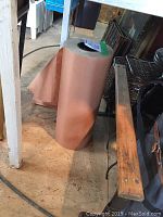 Large roll of brown waxed butcher paper sitting upright on a floor under a table.
