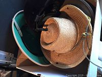 Photo of a box containing a light brown straw hat with a chin cord, a brown Stetson style wool hat, and a light-colored safari style hat.