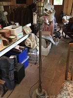 Full view of the floor lamp standing on the floor, showing stone base and brass pole in a cluttered room.