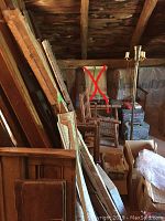 Room with assorted lumber, wooden chairs including a rocker and a floor lamp; some chairs marked not for sale with red markings