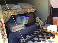 View inside trailer showing cane back sofa, cushioned chairs, blue-covered items, and storage bins.