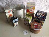 Wide view of all items: Proctor Silex crock pot, boxed kitchen gadgets including potato masher, chopper, slicer, grater, citrus cutter, and a holiday tin.
