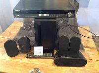 Full view of Samsung home theatre system components including DVD player, subwoofer, four satellite speakers, center speaker, and remote control on a wooden table.