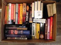 Box filled with hardcover books showing a variety of titles including fiction and religious texts.