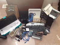 Photo of office supplies including keyboards, mouse, phones, clipboards, calculators, file holders, cables, and electronic devices