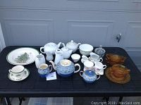 Multiple tea pots, creamers, sugar bowls, cups, and saucers arranged on table