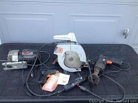 Lot includes multiple power tools laid out on black surface: scroll saw, circular saw, drill, screwdriver with charger, glue gun with sticks.